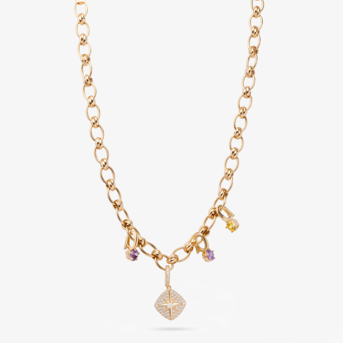 A delicate gold chain necklace featuring a central cluster of small charm pendants, including two purple gemstone charms, one yellow gemstone charm, and a larger diamond-patterned pendant at the bottom, displayed on a clean white background.